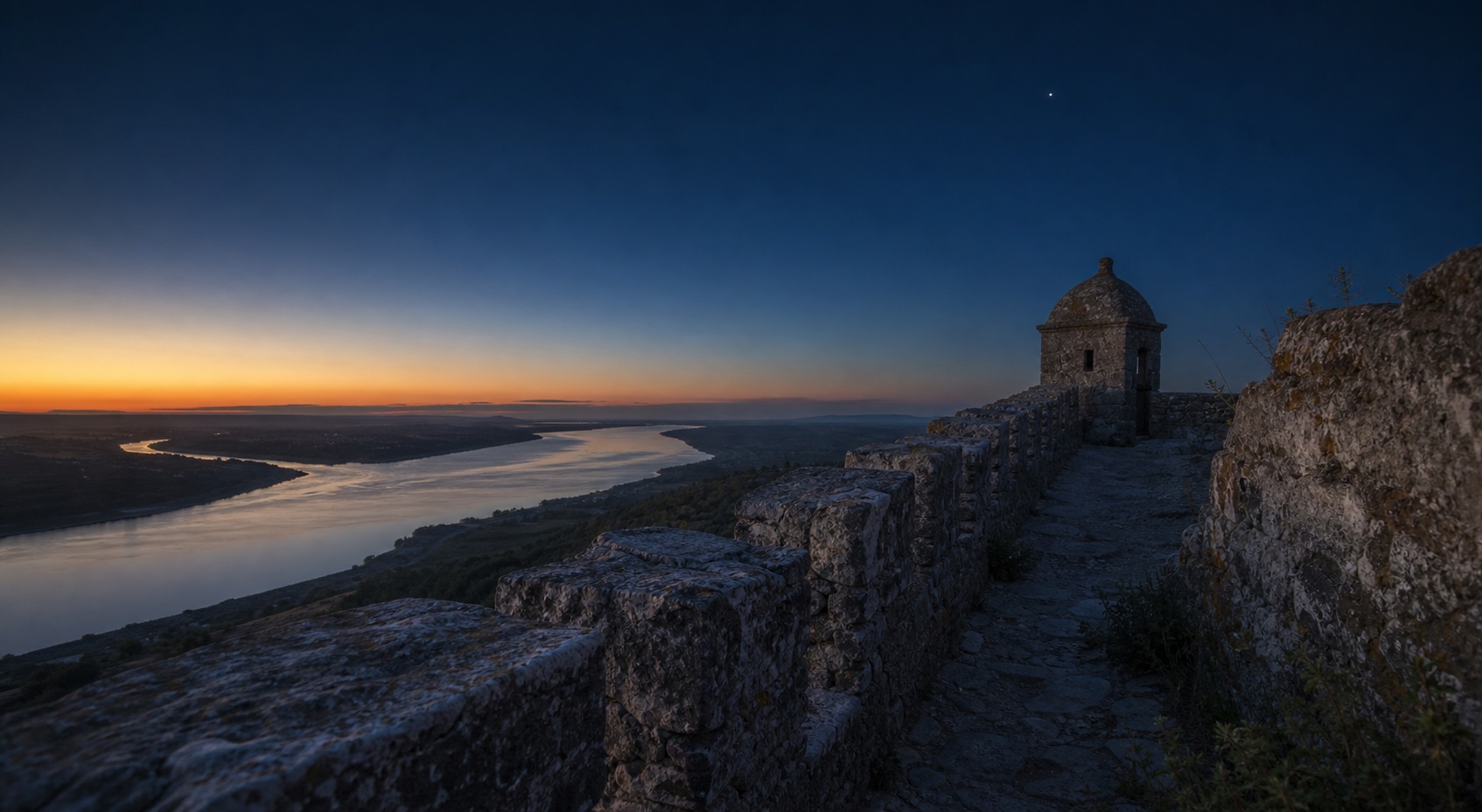 Castle ramparts overlooking a river valley at blue hour
